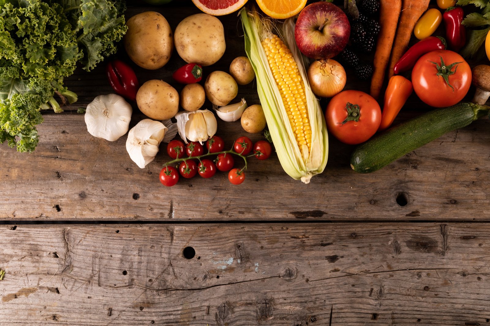 Overhead view of garlic with potatoes, corn and various fruits and vegetables on table